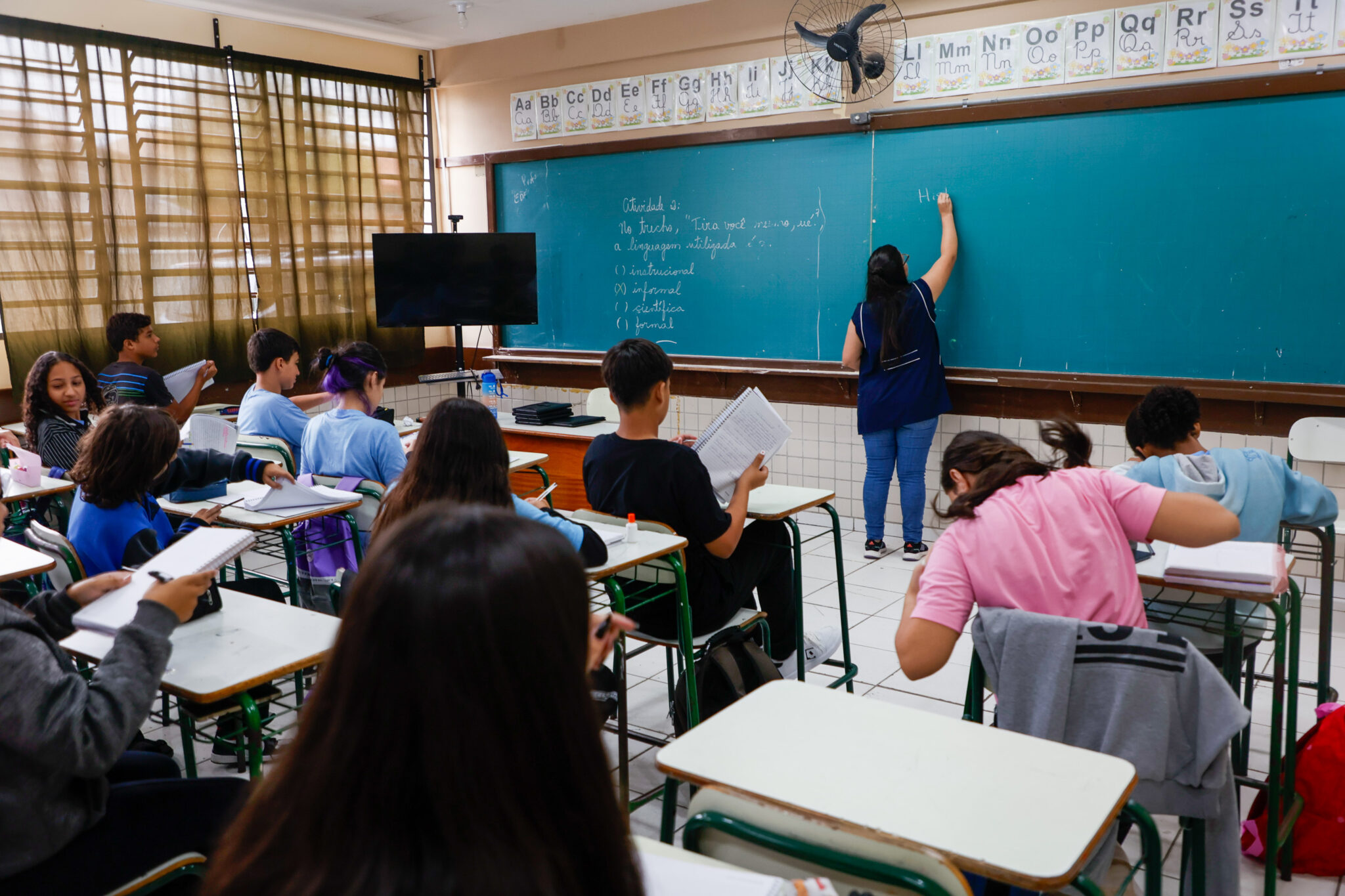 sala de aula com professora branca escrevendo no quadro